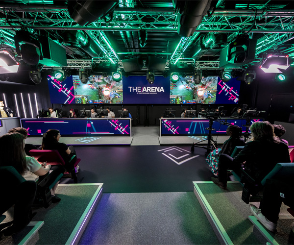 Students are broadcasting in the ambiently lit esports arena with viewers sitting in the audience
