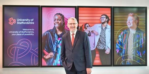 Suited man with hand in pocket stood in front of digital screens