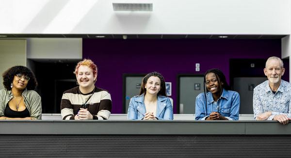 A group of diverse students casually dressed are standing up in the Science centre smiling for a photo