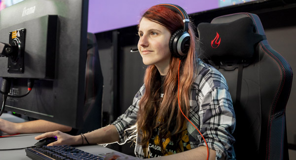 A young female student with long hair is wearing a gaming headset and using a computer in the Esports arena