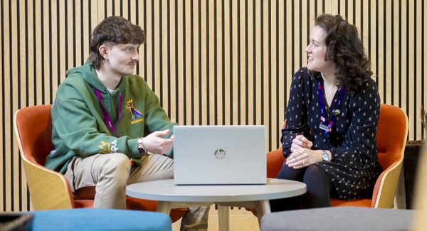 A male student is chatting to an advisor with a laptop