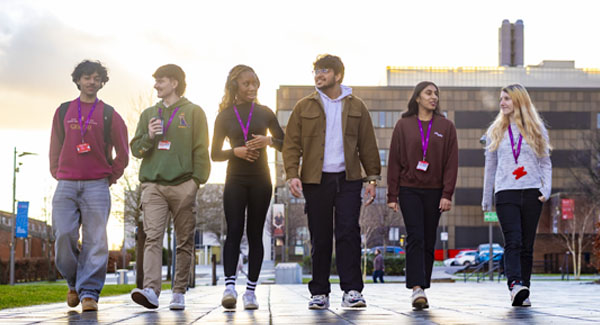 A group of 6 diverse young students dressed casually are chatting whilst walking on Leek Road campus
