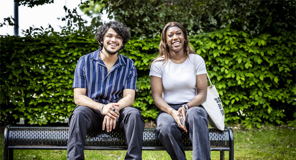 A male and female are smiling and sitting on a bench in a green space