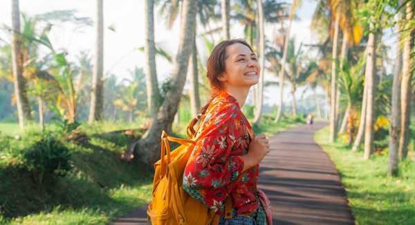 A female wearing a floral blouse carrying yellow rucksack is walking in nature in Bali