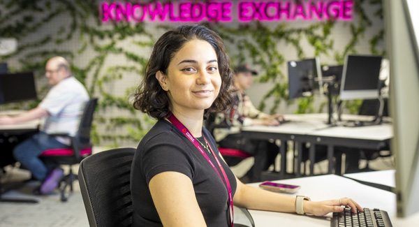 A female student is smiling and using a computer in a modern PC lab