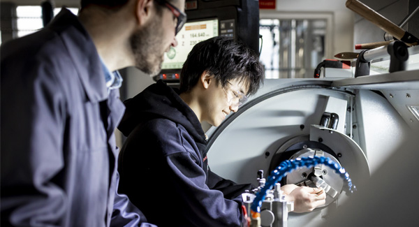 Two males wearing safety goggles are concentrating on using engineering equipment in the lab