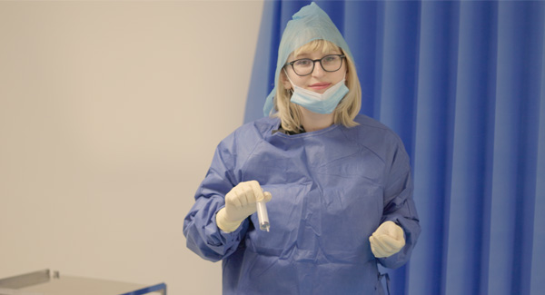 A female student with blonde hair is wearing blue scrubs uniform