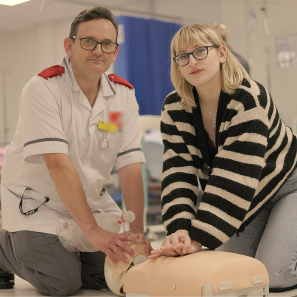 A lecturer wearing medical uniform and a student are performing CPR on a dummy